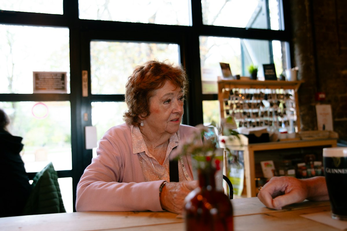 An older adult with reddish hair chatting at a cafe table
